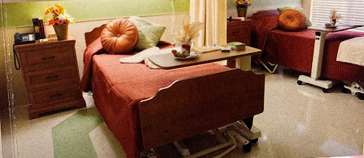 A cozy hospital room featuring a neatly made bed with colorful pillows and a bedside table.