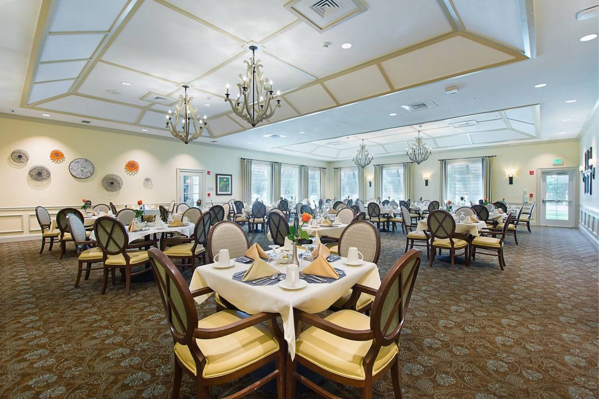 An elegant dining room setup with neatly arranged tables and chairs, featuring chandeliers and sophisticated decor.