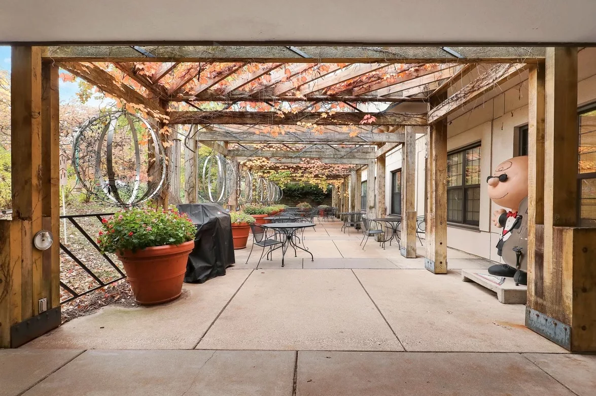 A cozy outdoor patio area with tables and chairs under a vine-covered pergola.