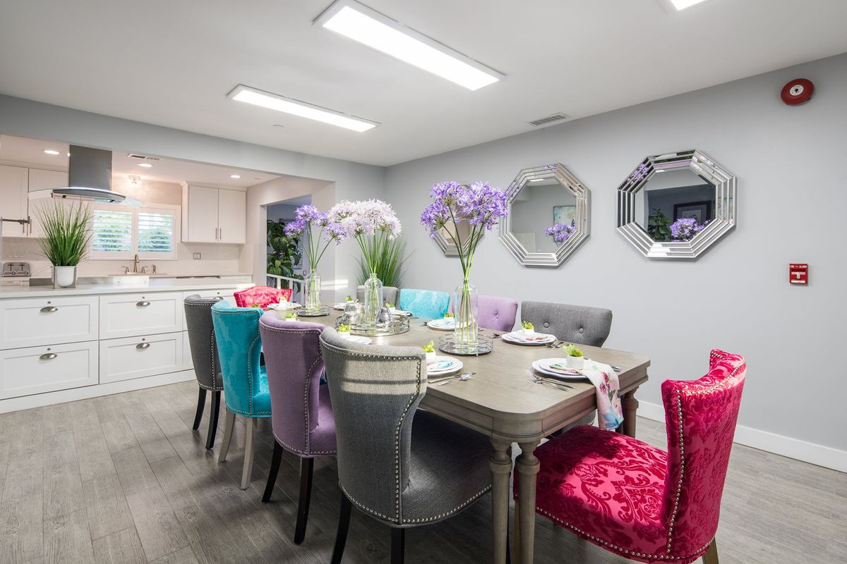 A modern dining room with a colorful array of chairs and a well-set table adorned with flowers.