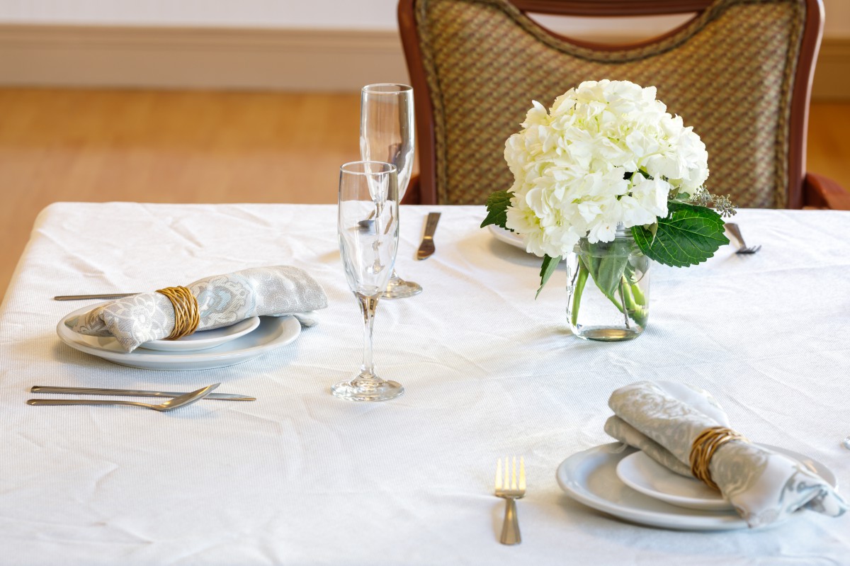 An elegantly set dining table with white hydrangea centerpiece, champagne glasses, and neatly arranged place settings.