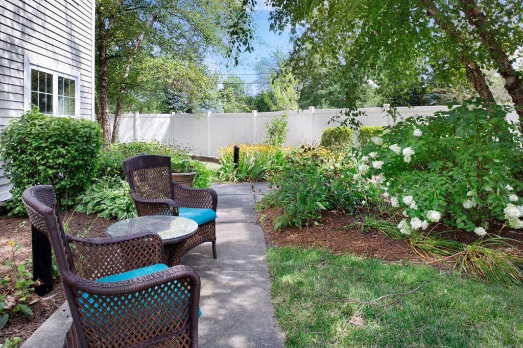 A serene garden with outdoor seating and a stone pathway surrounded by lush greenery and flowers.