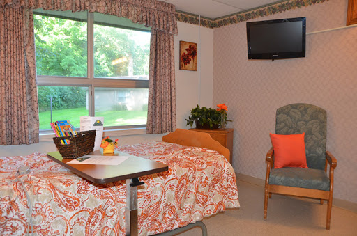 A cozy hospital room featuring a neatly made bed, a comfortable chair, and a view through the window.