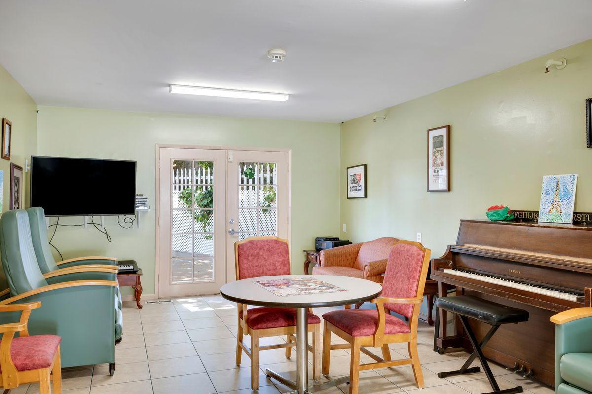 A cozy living room with a piano, television, table, and chairs.
