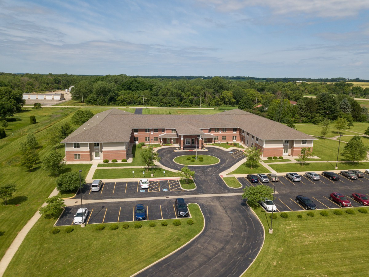Aerial view of a large building with surrounding greenery and parking areas.