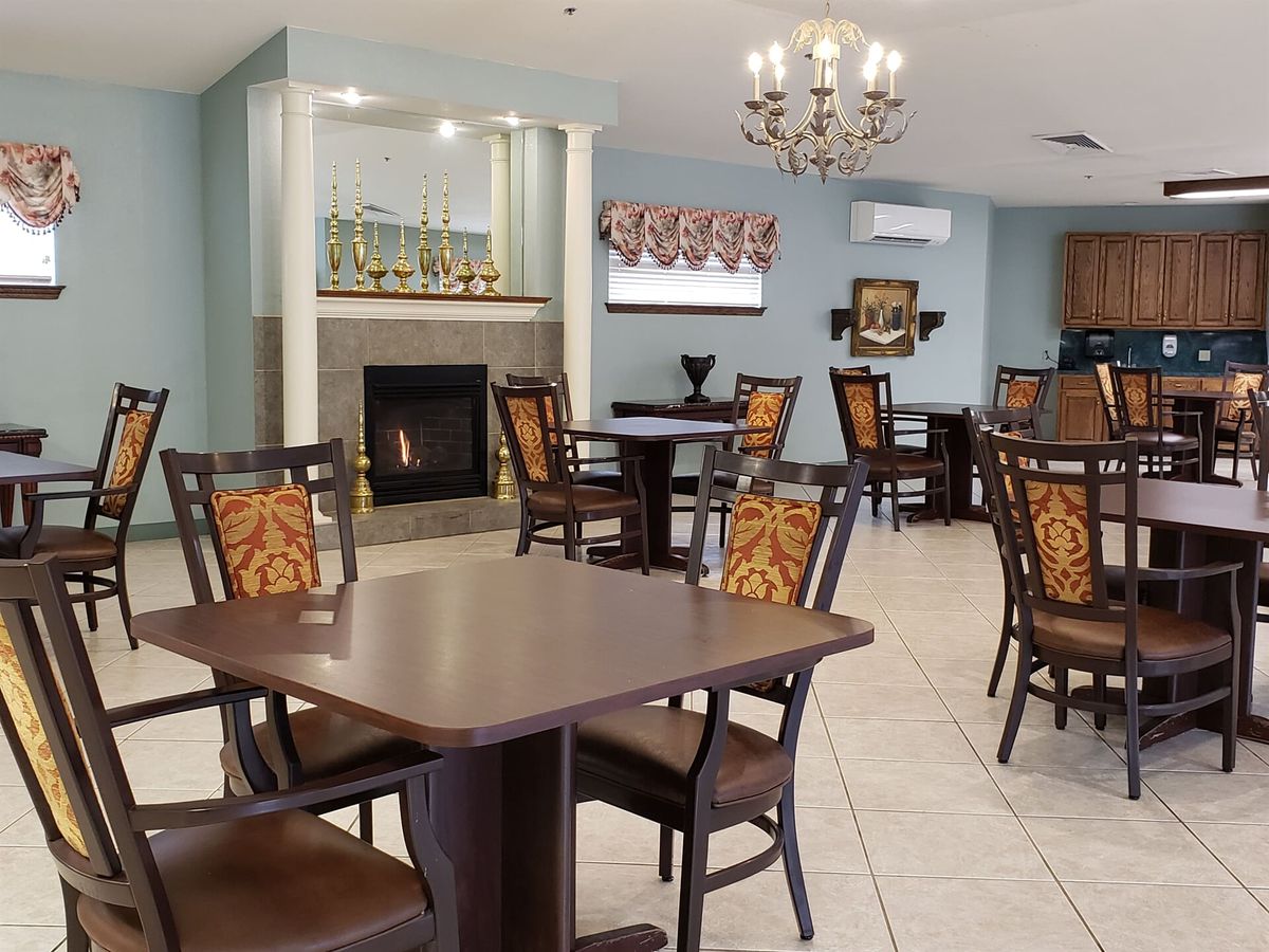 A cozy dining area with neatly arranged tables and chairs, featuring a fireplace and decorative chandelier.