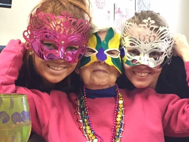 Three people wearing colorful masks and festive costumes pose together for a celebration.