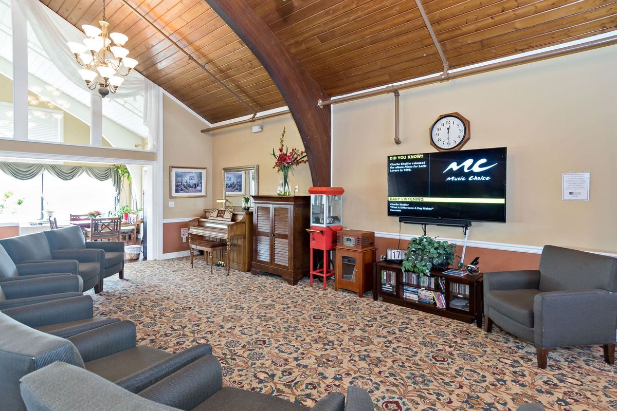 A cozy living room with a wooden ceiling, featuring a piano and a television.