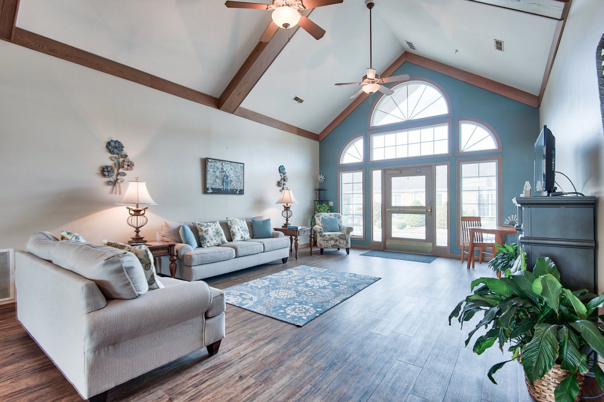 A spacious living room with vaulted ceiling, featuring comfortable sofas, a rug, and large windows letting in natural light.