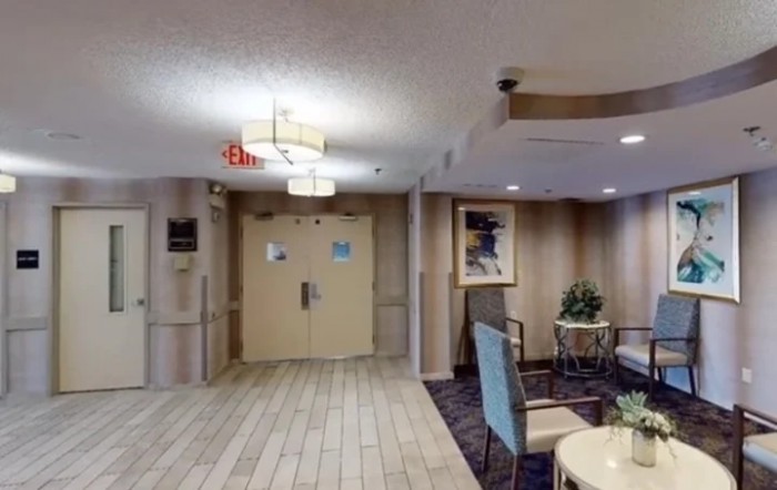 A lobby with seating and decor, featuring an exit sign and overhead lighting.