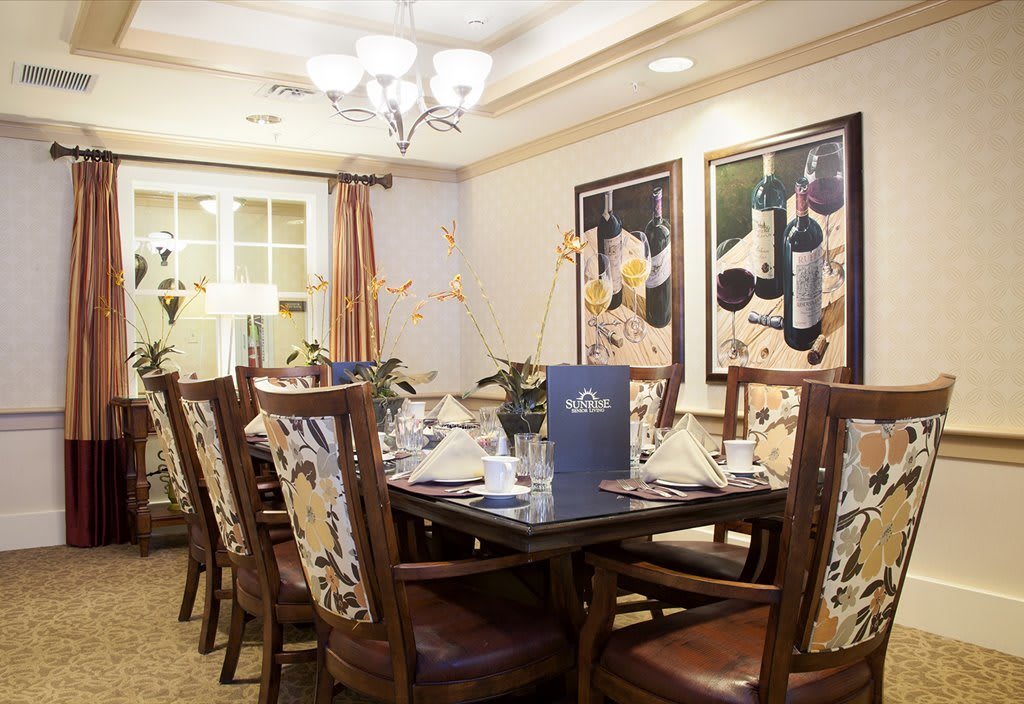 A well-decorated dining room featuring a set of elegant chairs and table, illuminated by a chandelier, with wine-themed paintings on the walls.