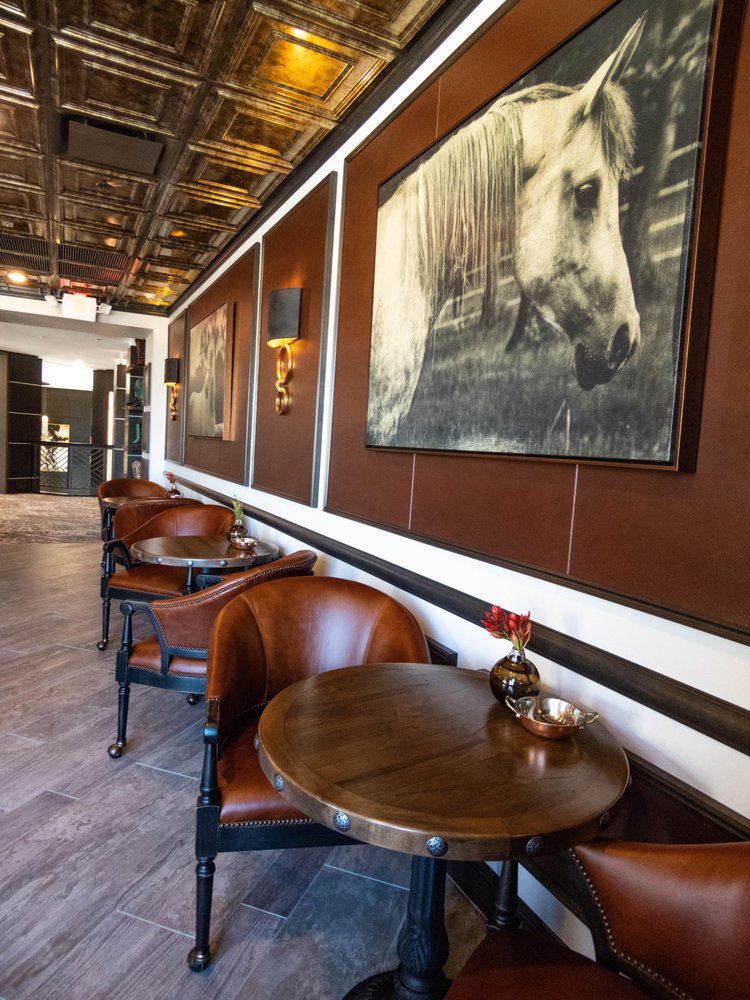 A cozy cafe interior featuring leather chairs, wooden tables, and horse-themed artwork on the walls.