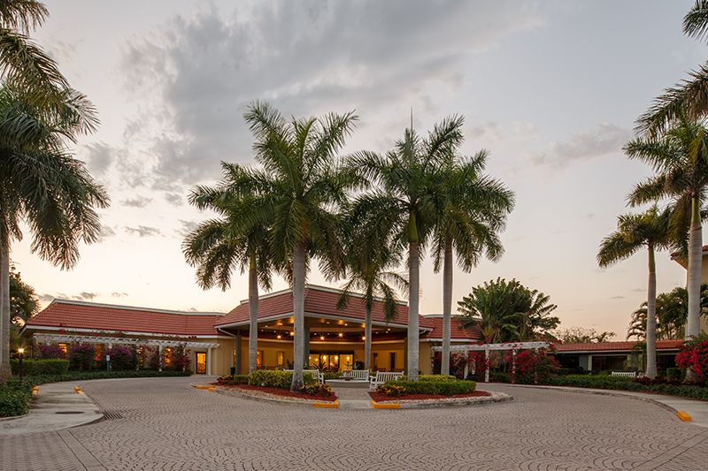 A tropical building surrounded by palm trees at sunset.