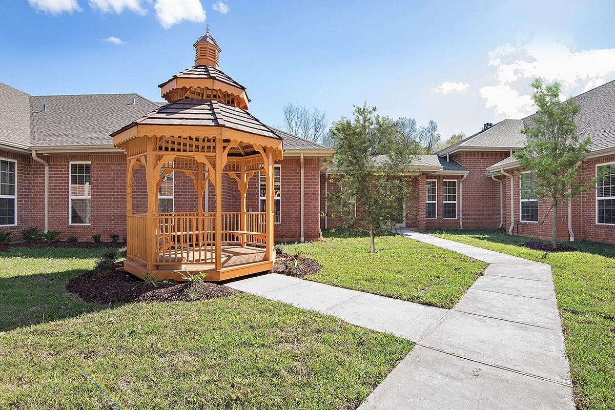 A wooden gazebo in front of a brick building with landscaped pathways and lawn.