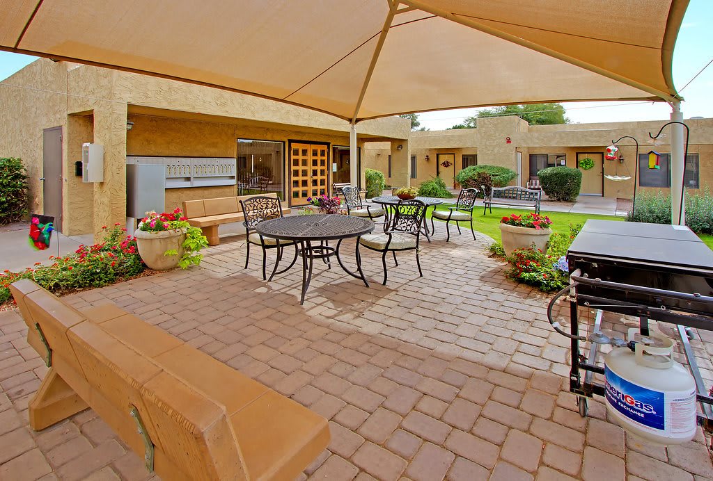 A cozy outdoor patio featuring a shaded seating area with metal furniture surrounded by a well-maintained garden.