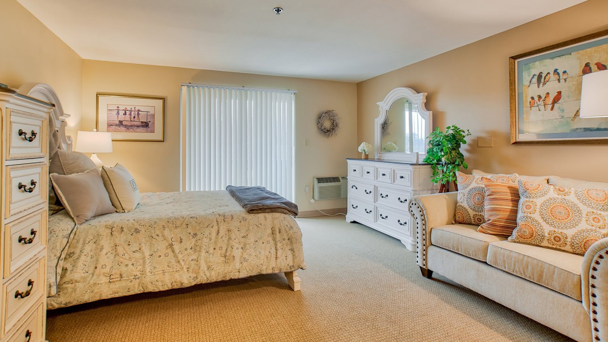 A cozy bedroom featuring a bed, sofa, dresser with a mirror, and decorative elements.