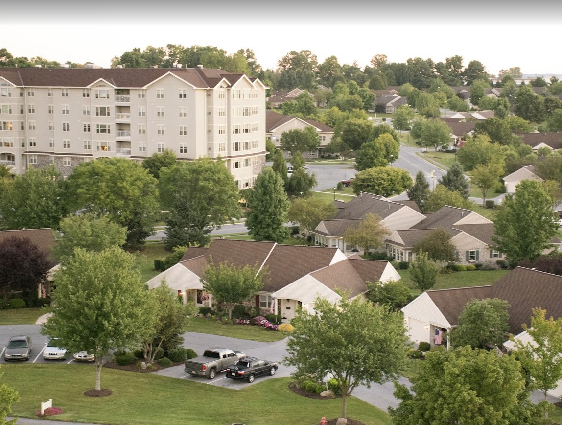 A suburban neighborhood with houses and an apartment building surrounded by trees and greenery.