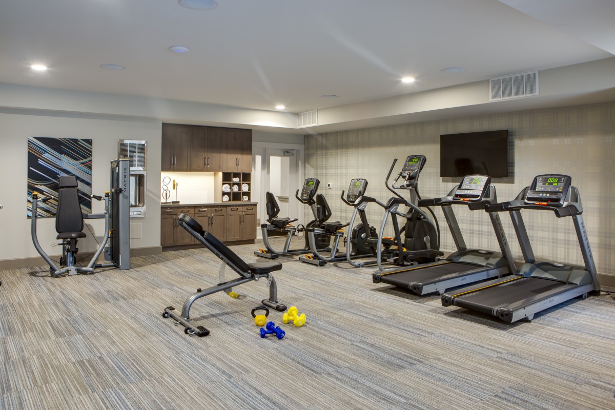 A modern gym with various fitness equipment including treadmills, stationary bikes, and dumbbells.