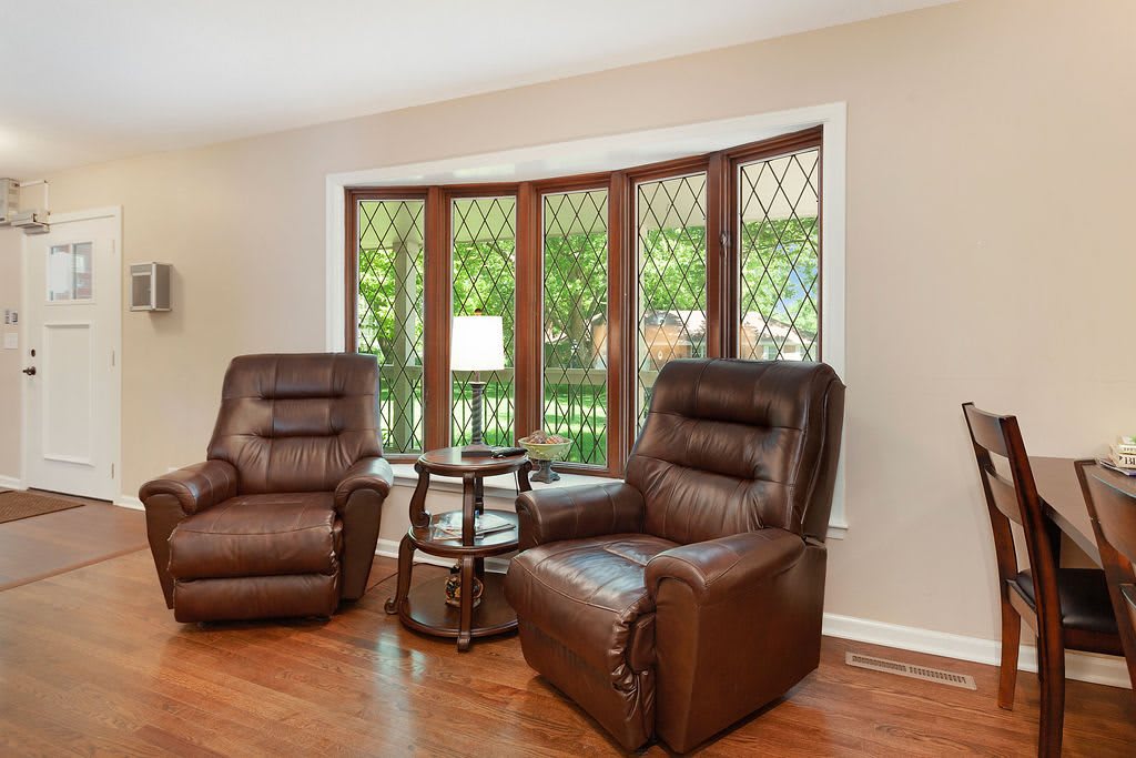 A cozy living room with two brown recliner chairs facing a bay window, complemented by wooden flooring.