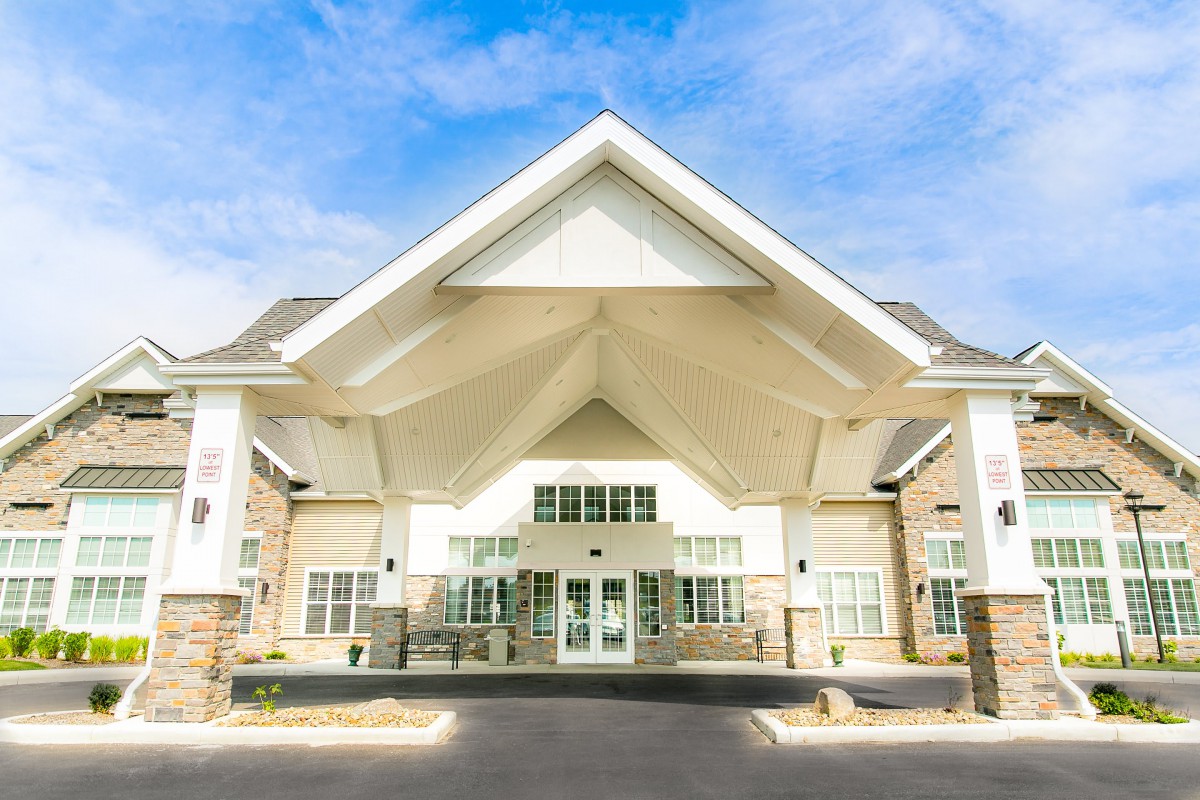 A grand entrance of a modern building with a large overhanging roof and multiple windows.