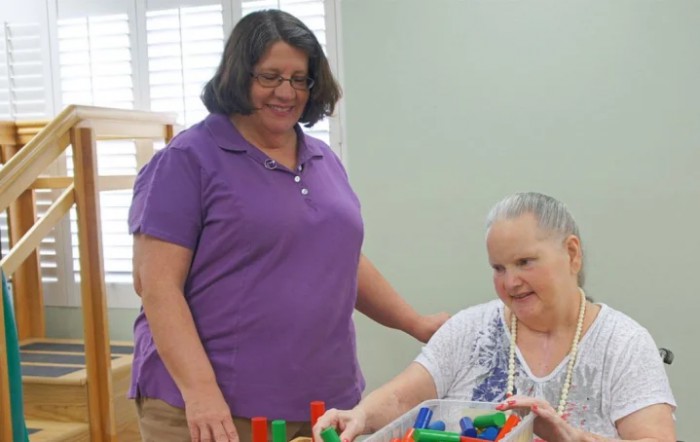 A caregiver assisting a woman with an activity using colorful blocks.