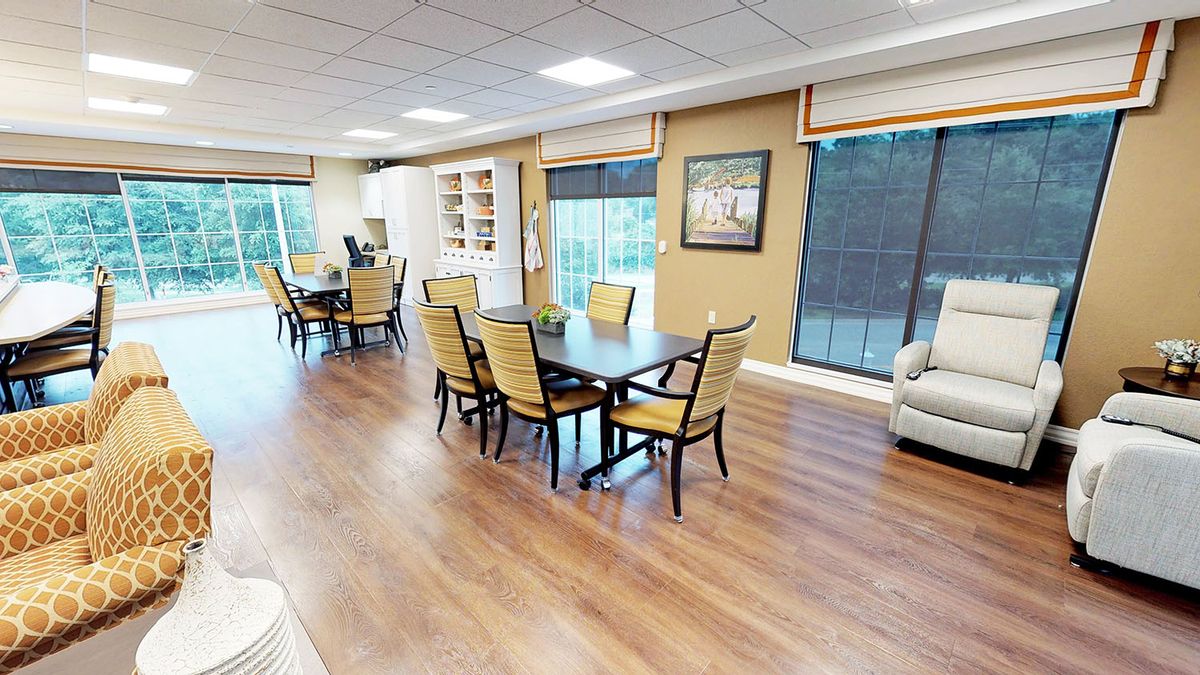 A spacious dining area with multiple tables and chairs, featuring large windows and a hardwood floor.