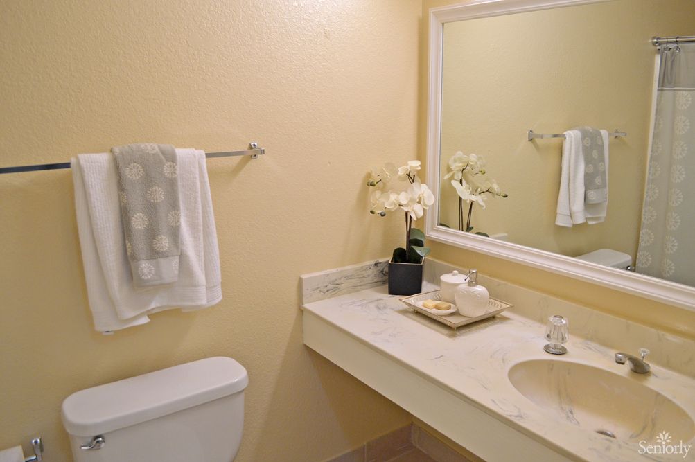 A neatly organized bathroom with a large mirror, countertop, and decorative flowers.