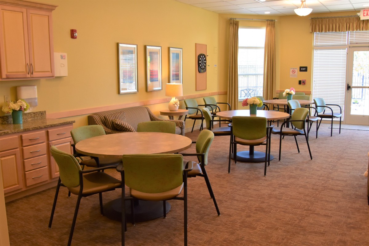 A cozy lounge area with tables, chairs, and a sofa arranged on a carpeted floor.