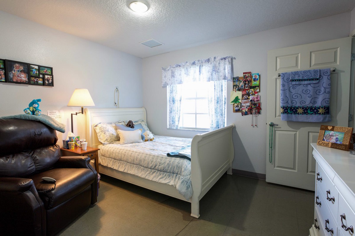 A cozy bedroom with a white bed, bedside lamp, and a window letting in natural light.