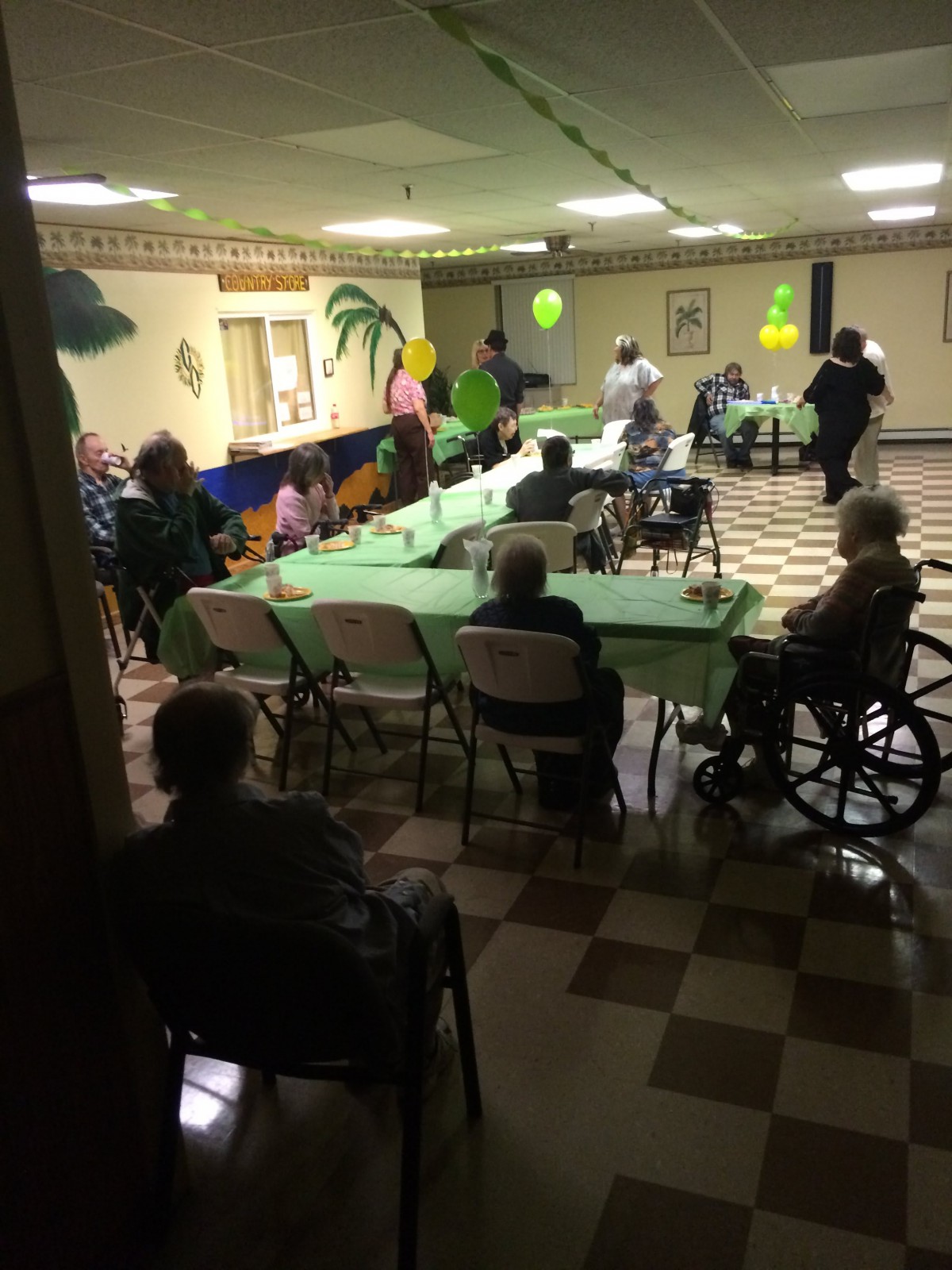A group of senior citizens gathered for a party in a decorated indoor space with balloons and tables.