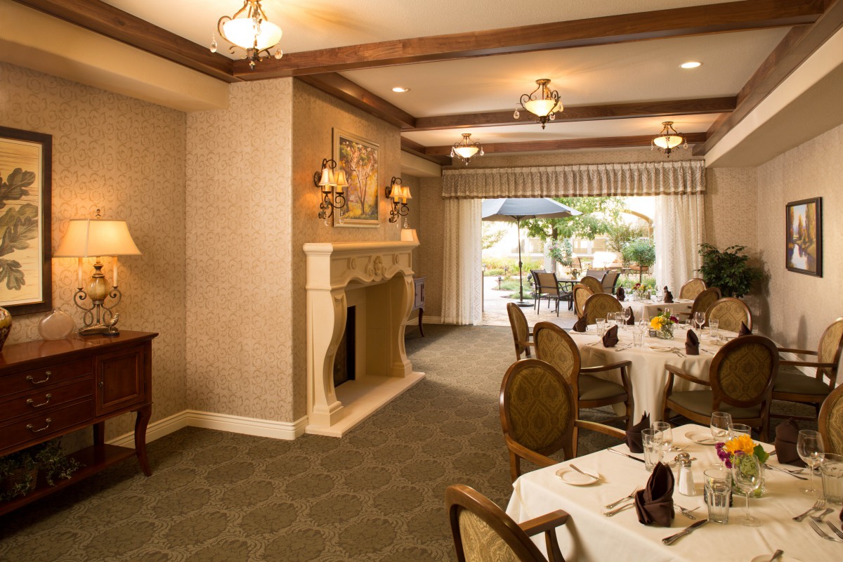 An elegant dining room with a fireplace, chandeliers, and neatly arranged tables and chairs.