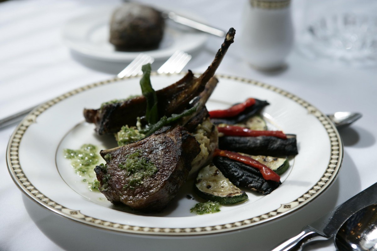 A gourmet dish featuring lamb chops served with asparagus, zucchini, and red peppers.