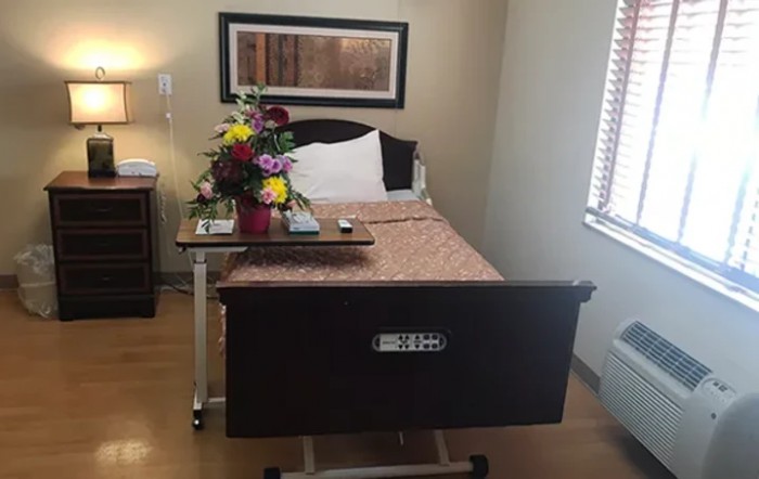A hospital room with a neatly made bed and a bouquet of flowers on the bedside table.