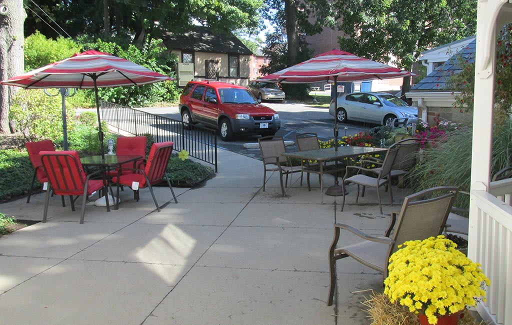 A cozy outdoor patio with tables, umbrellas, and a view of a red SUV parked nearby.