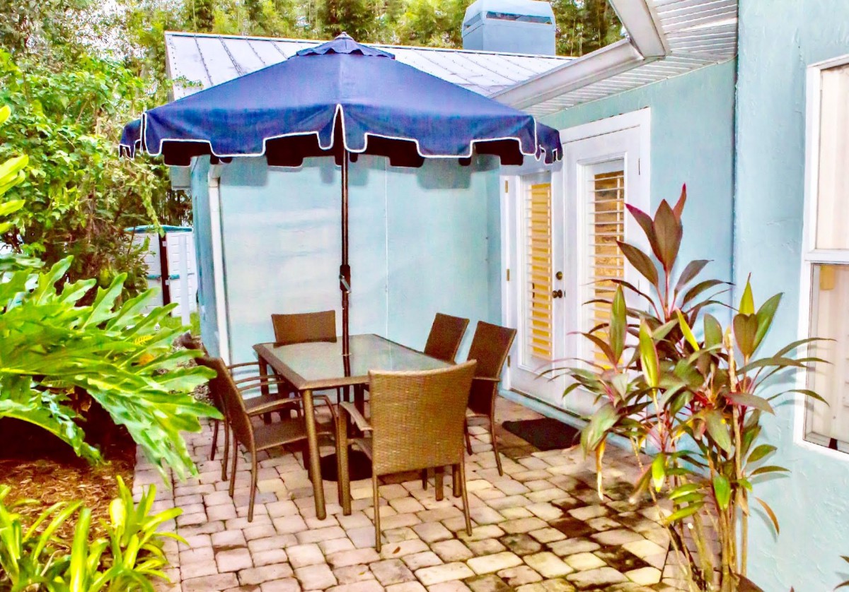 A cozy patio setup with a table, chairs, and an umbrella surrounded by lush plants.