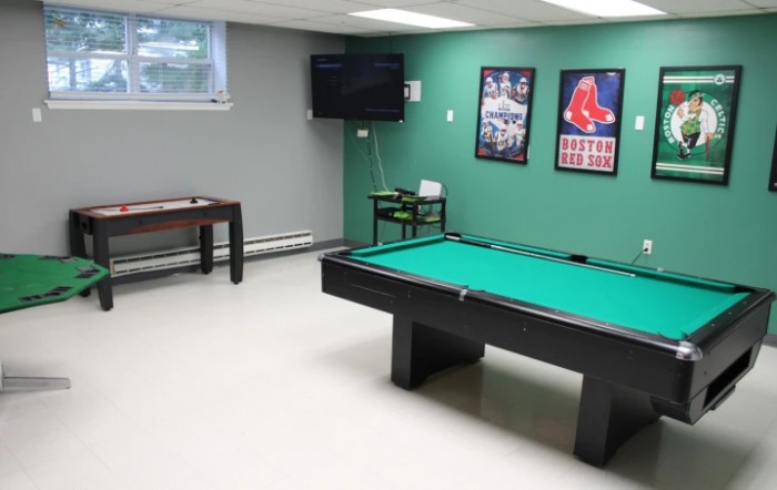 A game room featuring a billiards table, foosball table, and wall-mounted television with sports posters.