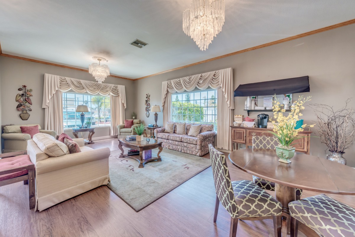 A spacious and elegantly decorated living room with chandeliers, comfortable sofas, and large windows adorned with decorative curtains.