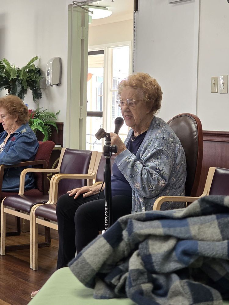 An elderly woman seated in a waiting area, holding a cane.