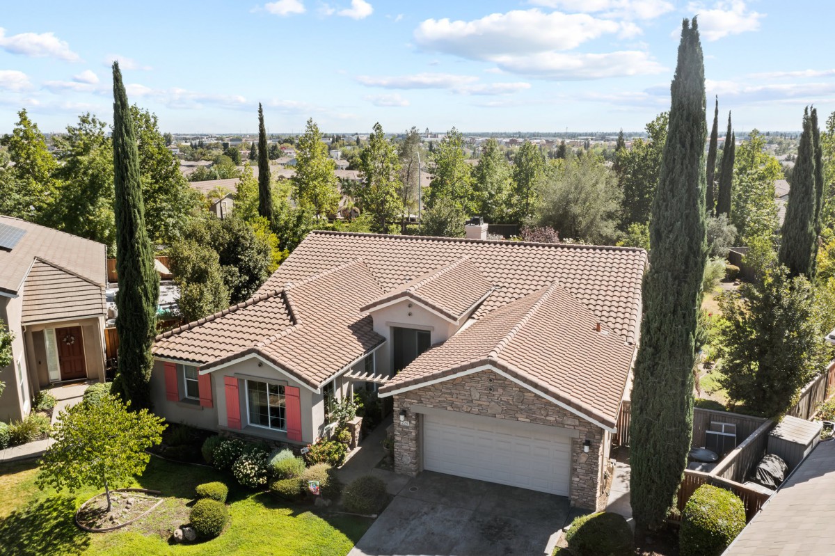 Aerial view of a residential house with a tiled roof, surrounded by trees and a well-manicured garden.