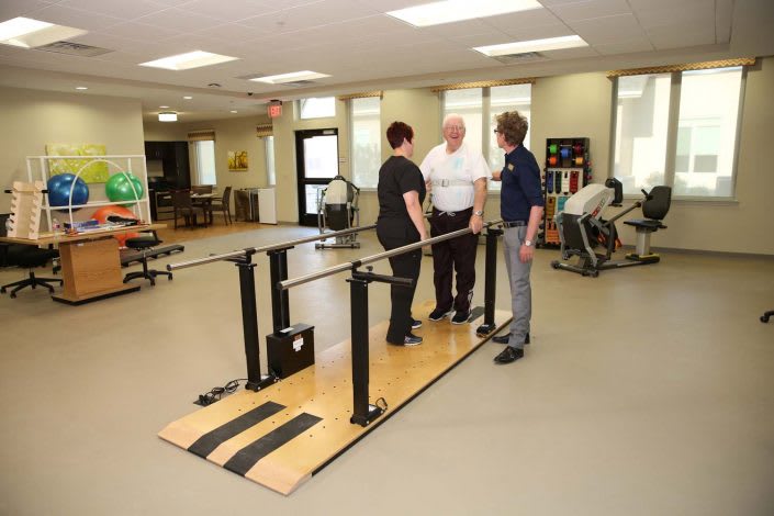 A physical therapy session in progress, featuring therapists assisting a patient using parallel bars.