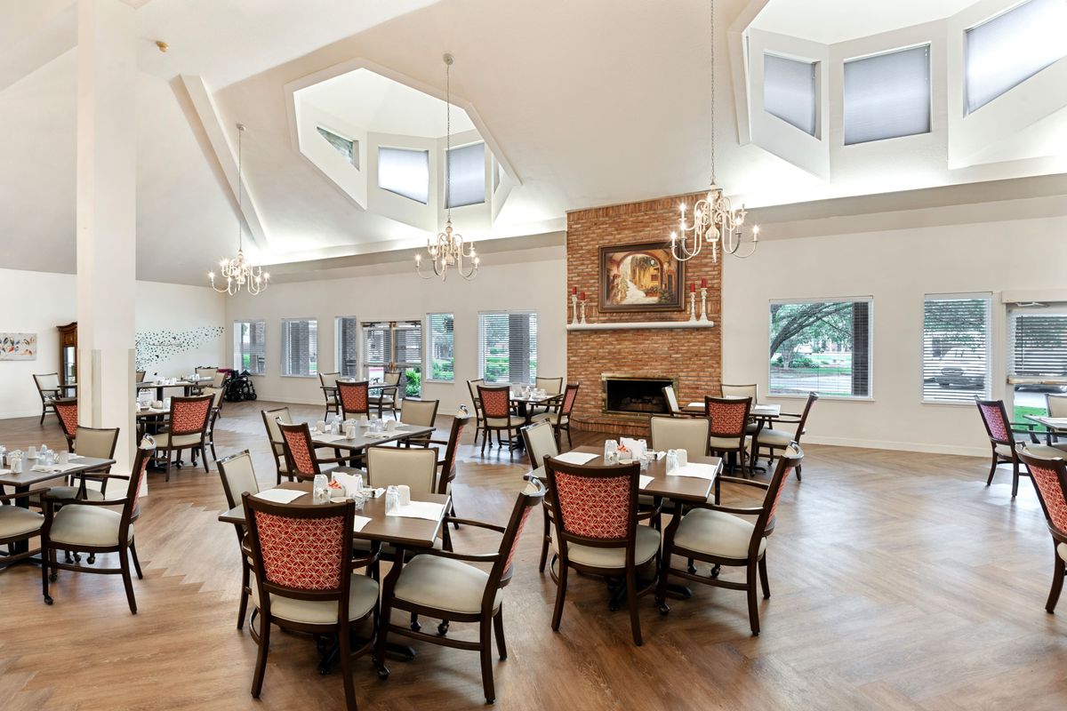 A spacious dining area with multiple tables and chairs, featuring a brick fireplace and large windows.