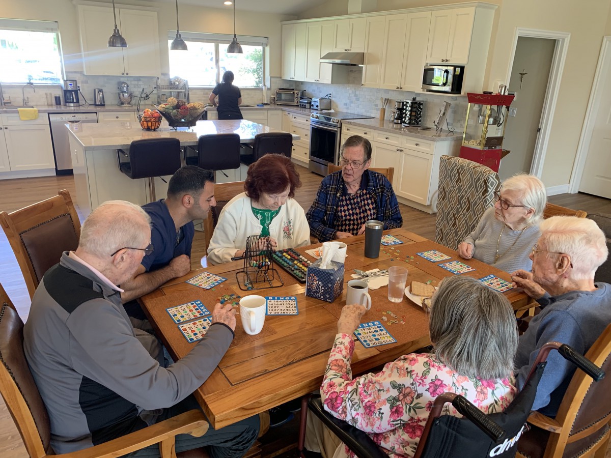 A group of seniors gathered around a table playing cards in a kitchen setting.