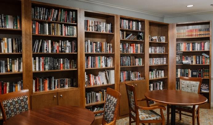A cozy library corner with wooden bookshelves filled with books, accompanied by chairs and tables for reading.