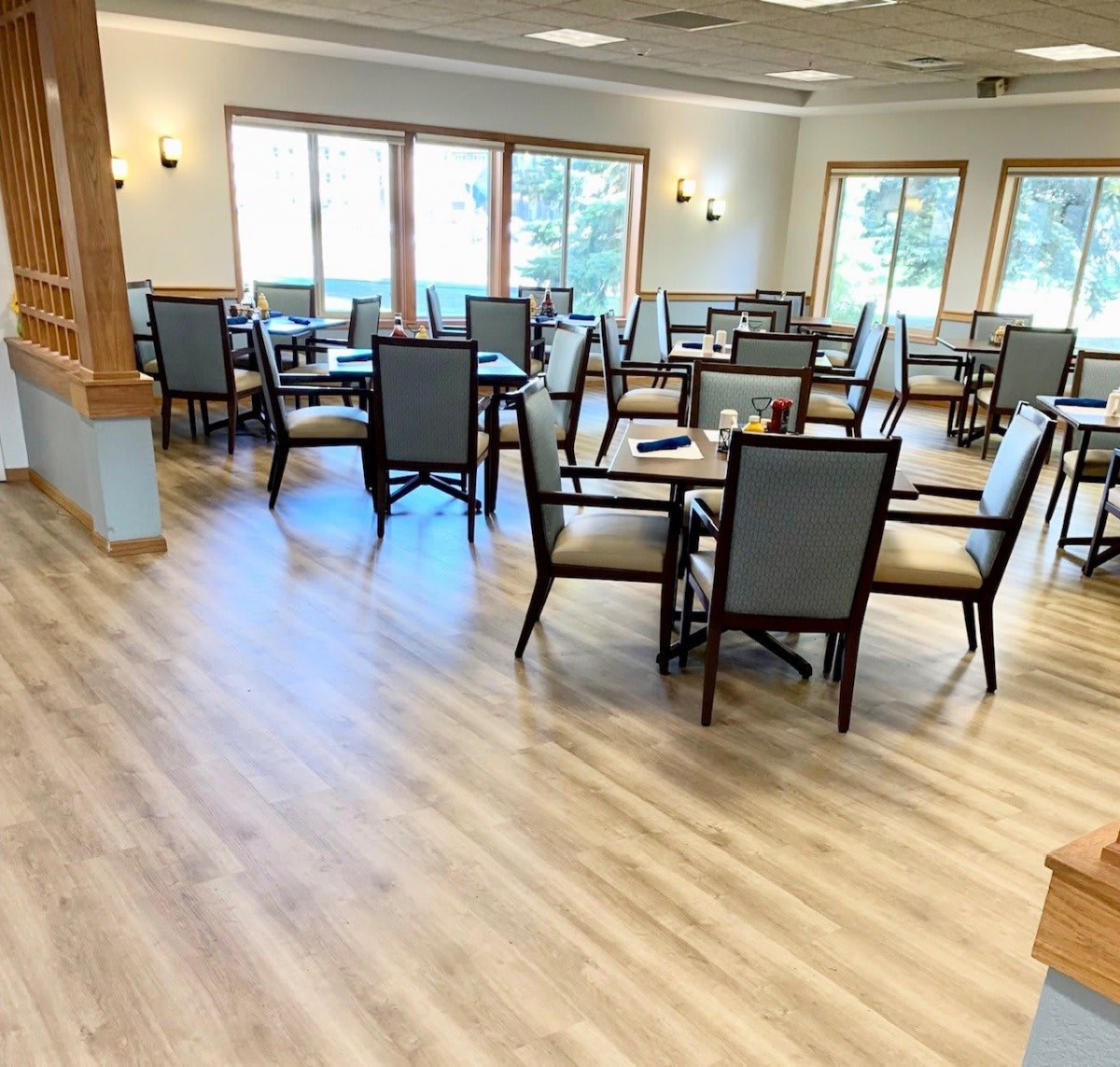 A bright and spacious dining room with multiple tables and chairs, featuring a wooden floor.
