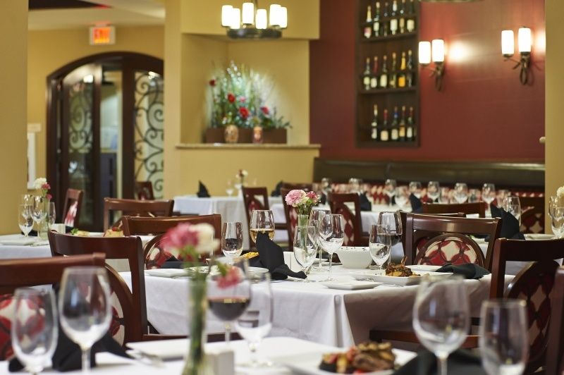 A beautifully set dining area in an elegant restaurant with neatly arranged tables and wine bottles displayed on the wall.