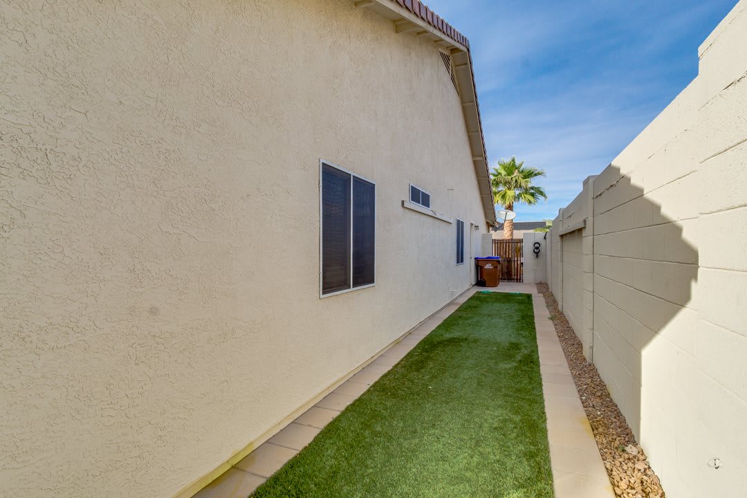 A side yard featuring artificial turf alongside the exterior wall of a house, bordered by a fence.