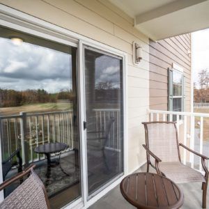 A cozy balcony with two chairs and a small table, featuring a sliding glass door and scenic view.