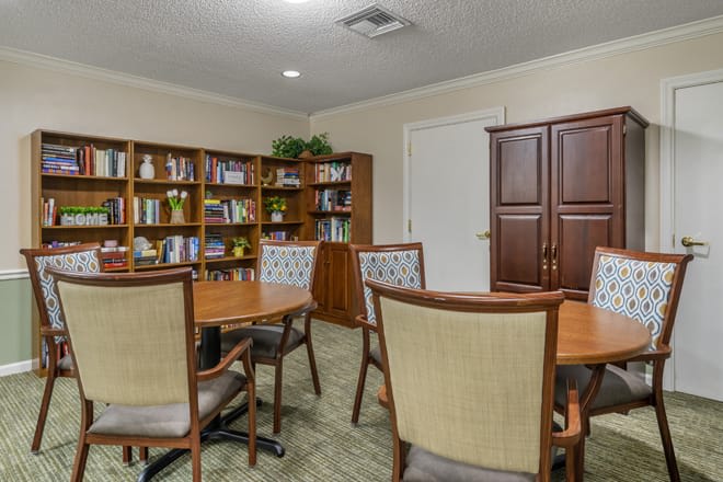 A quiet library room with shelves of books, tables, and chairs arranged for meetings or study.