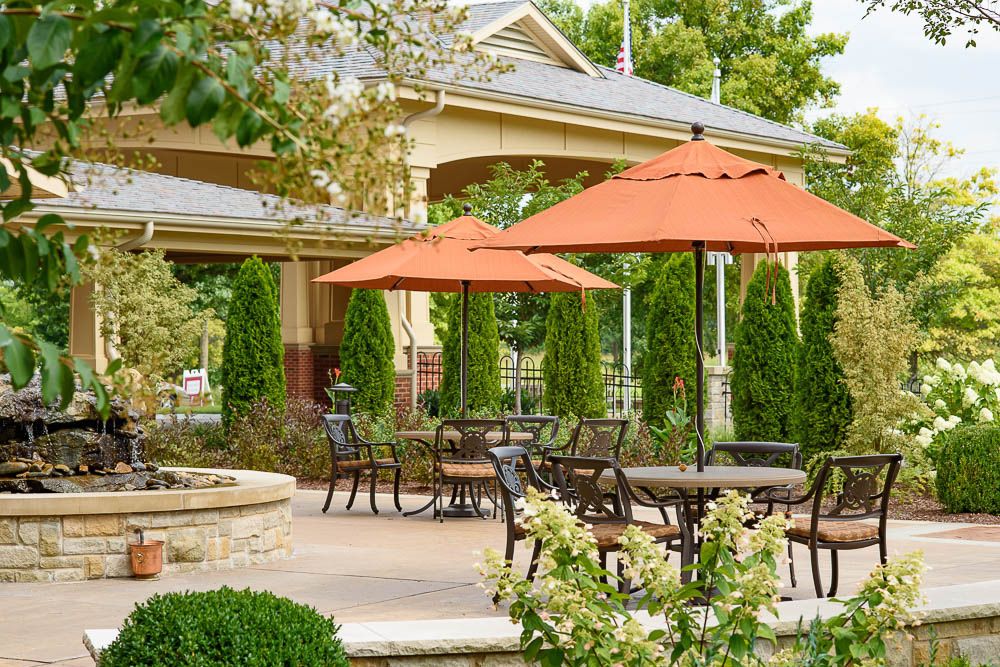 A tranquil outdoor patio area with tables and orange umbrellas, surrounded by lush greenery.