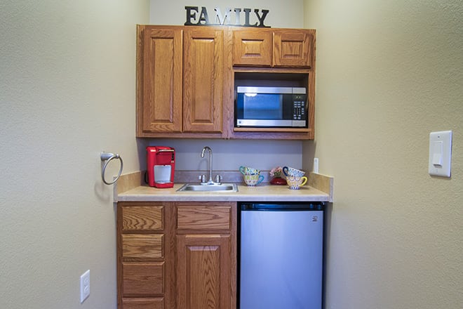 A compact kitchenette with wooden cabinets, a microwave, mini fridge, coffee maker, and small sink.
